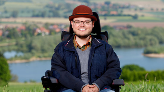 Constantin Grosch mit rotem Hut und blauer Jacke steht vor den Weser-Auen